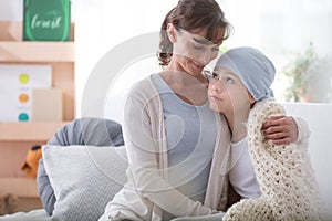 Smiling caregiver supporting sick child with cancer wearing blue headscarf