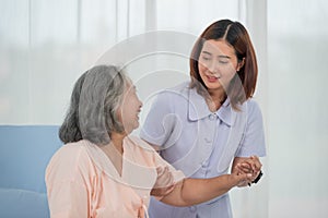 Smiling caring Asian doctor supporting holding hand of olde senior female patient lying on bed at clinic or hospital