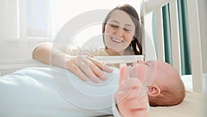 Smiling caring and loving mother stroking her little baby in cradle. Concept of parenting, family happiness and baby