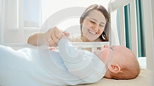 Smiling caring and loving mother stroking her little baby in cradle. Concept of parenting, family happiness and baby
