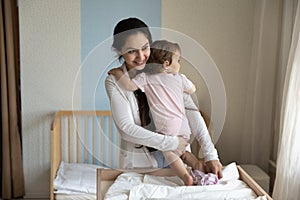 Smiling caring young mother changing baby clothes, diaper on table