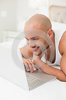 Smiling casual bald man using laptop in bed