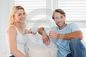 Smiling casual couple sitting on couch having coffee