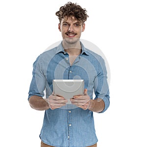 Smiling casual guy in denim shirt holding tab