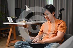 Smiling man sitting on sofa and using laptop computer.