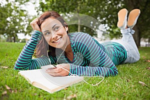 Smiling casual student lying on grass listening to music