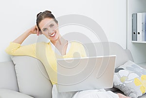 Smiling casual woman with laptop sitting at home