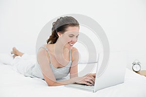 Smiling casual woman using laptop in bed