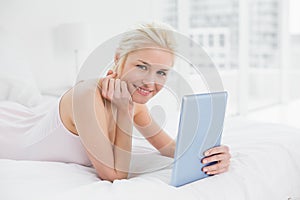 Smiling casual young blond with tablet PC in bed