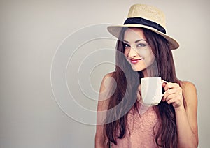 Smiling casual young woman with cup of coffee looking happy in straw hat on blue background