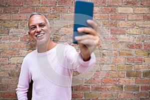 Smiling caucasian adult man taking selfie. Orange brick wall background. Copy space.