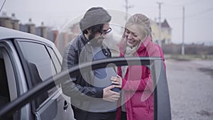 Smiling Caucasian blond woman caressing her husband`s pregnant belly and imitating listening baby hitting. Cheerful