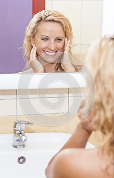 Smiling Caucasian Blond Woman Looking in Mirror and Examining Her Face