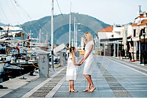 Smiling caucasian blonde  mother and daugher walking by harbor with yachts on a touristic sea resort