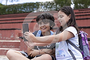 Smiling caucasian boy and girl elementary school students taking a picture together with a smart phone before going to class