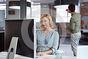 Smiling caucasian businesswoman sitting at desk using computer with male colleague in background