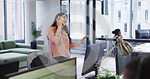 Smiling caucasian businesswoman standing and talking using phone headset and computer in busy office