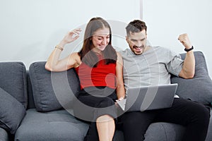 Smiling Caucasian Couple love relaxing and funny in online games with laptop in social media technology on sofa. Work from home