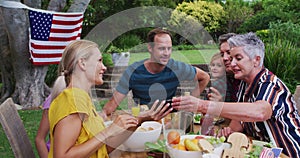 Smiling caucasian family having celebration meal in garden looking at smartphone together
