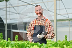 Smiling caucasian farmer holding digital tablet standing in hydroponics greenhouse plantation. Agriculture technology