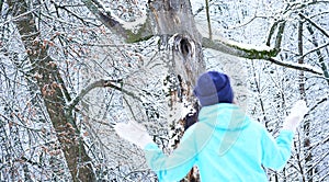 Smiling Caucasian girl in gray knitted mittens and a hat. Snowy forest in the background. Winter. Snow around.