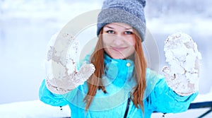Smiling Caucasian girl in gray knitted mittens and a hat. Snowy forest in the background. Winter. Snow around.