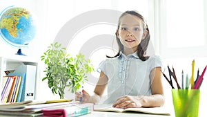 Smiling caucasian girl sitting at desk in class room and looking at workbook. Portrait of young schoolgirl studying at