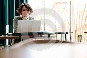 Smiling caucasian girl working with laptop while sitting in cafe