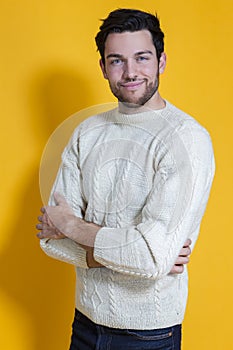 Smiling Caucasian Handsome Man In knitted White Striped Sweater Posing Against Yellow Background While Smiling Happily With Hands