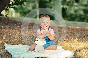 Smiling Caucasian happy baby girl sitting on blanket on ground outdoors in autumn fall park. Funny cute adorable kid child