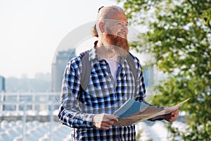 Smiling caucasian hipster bearded man having trip. Smiling male traveler walking with map on weekends. Travel concept