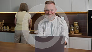 Smiling Caucasian man retired adult mid aged businessman husband typing on laptop computer working online shopping