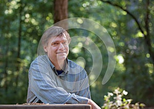 Smiling Caucasian man sitting alone at wooden table in forest