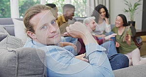 Smiling caucasian man sitting with diverse group of happy friends socialising in living room