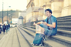 Smiling caucasian man using mobile phone while sitting on steps â€“ happy tourist searching for map directions on smartphone