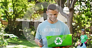 Smiling caucasian man wearing volunteer t shirt holding recycling crate, collecting plastic waste