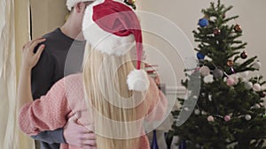 Smiling Caucasian man and woman waltzing in front of New Year tree at home. Happy young couple spending time together on