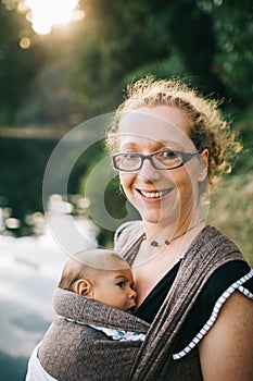 Smiling caucasian mom holding her colored child in a sling