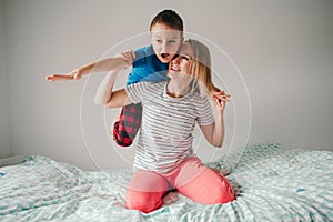 Smiling Caucasian mother and boy son playing in bedroom at home. Child sitting on moms shoulders and laughing. Family having fun