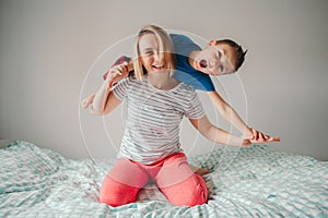 Smiling Caucasian mother and boy son playing in bedroom at home. Child sitting on moms shoulders and laughing. Family having fun