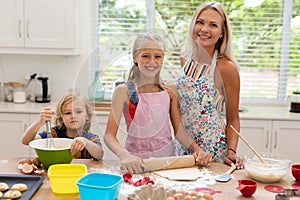 Smiling caucasian mother, daughter and son wearing aprons baking cookies together in kitchen