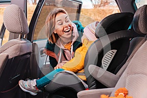 Smiling caucasian mother prepares her little cute child for a trip by car. View inside a car