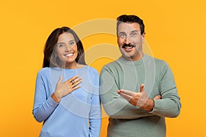 Smiling caucasian old woman holds her hand on chest in gratitude as man gestures openly towards