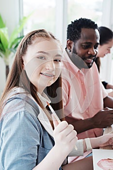 Smiling Caucasian studens girl is holding paintbrush for drawing and painting with watercolor for art with African teacher man in