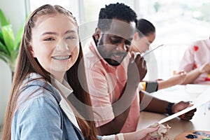 Smiling Caucasian studens girl is holding paintbrush for drawing and painting with watercolor for art with African teacher man in