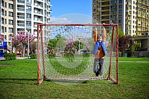 Smiling Caucasian teenage boy hanging on a soccer football goal on a playground near his house. Active leisure for children