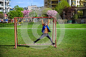 Smiling Caucasian teenage boy hanging on a soccer football goal on a playground near his house. Active leisure for children