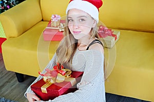 Smiling Caucasian Teenage lovely girl wearing red hat of Santa Claus and holding a big red gift box in Christmas and birthday