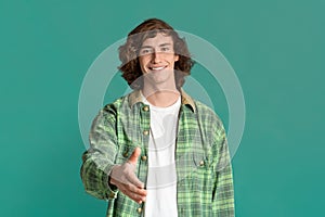 Smiling Caucasian teenager holding out his hand for handshake on turquoise background