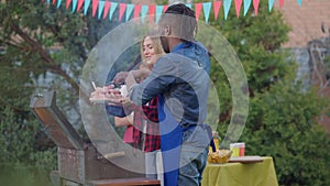 Smiling Caucasian woman bringing raw meat to African American man cooking bbq grill. Happy interracial husband and wife